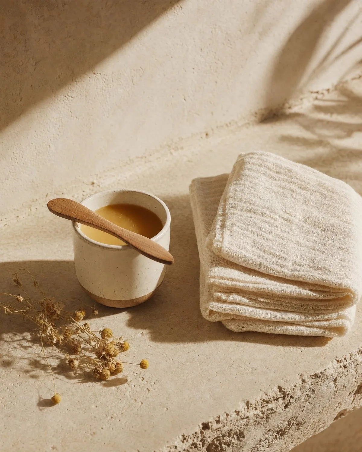 Ceramic pot of warm wax beside folded linen cloths